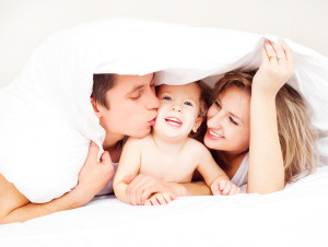 happy family, mother ,father and their baby under the blanket on the bed at home (focus on the man)